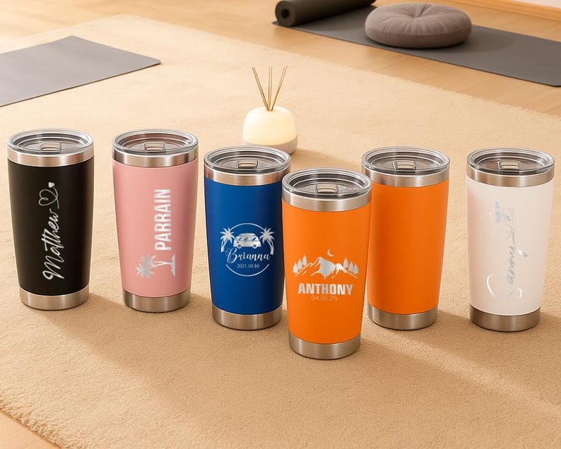 May include: A collection of six stainless steel insulated tumblers with silver lids. The tumblers are in various colors, including black, pink, blue, and orange. Each tumbler has custom text or graphics, such as names and dates, making them personalized gifts.