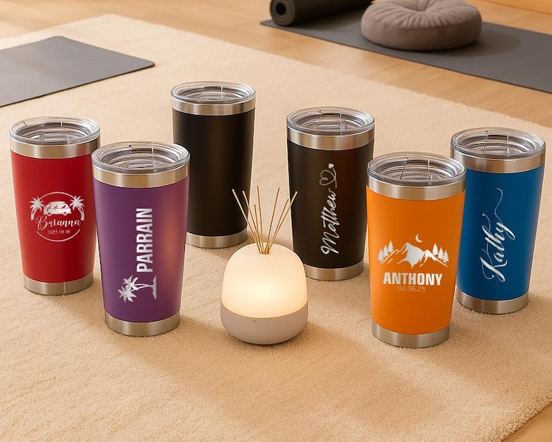 May include: A collection of insulated tumblers in various colors, including red, purple, black, orange, and blue. Each tumbler has a silver lid and base. Some tumblers feature personalized text and graphics, such as names and dates, making them ideal for gifts.