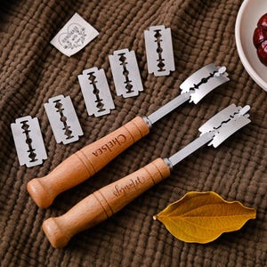Può includere: Due lame per pane con manico in legno e lame in acciaio inossidabile e diverse lame di ricambio. I manici sono incisi con nomi. Sono presenti anche una foglia secca e una piccola etichetta con la scritta "Handmade with love".