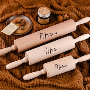 May include: Three wooden rolling pins with the name "Miriam" engraved on them. The rolling pins are of different sizes and are arranged on a brown fabric background.