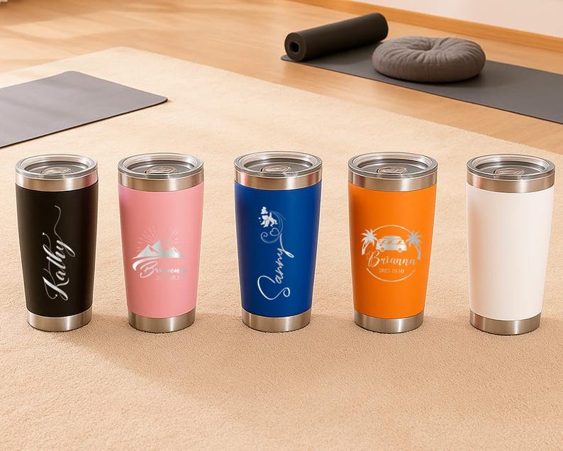 May include: Five stainless steel insulated tumblers in black, pink, blue, orange, and white. Each tumbler has a silver lid and base. The black tumbler has the name "Kathy" in a cursive font. The other tumblers have custom designs and names.