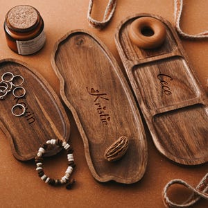 Puede incluir: Tres bandejas de servir de madera con nombres personalizados "Kristie", "Coco" y "Kevin". Las bandejas son de madera oscura y tienen un aspecto natural y rústico. Cada bandeja tiene una forma y un diseño únicos.