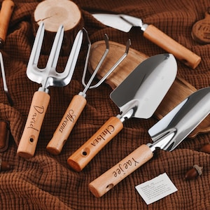 May include: Set of five gardening tools with wooden handles. The tools include a trowel, a hand rake, a cultivator, a small hand rake, and a small shovel. Each tool has a different name engraved on the handle: David, Juliana, Chelsea, Ya'yee, and  '1881'.