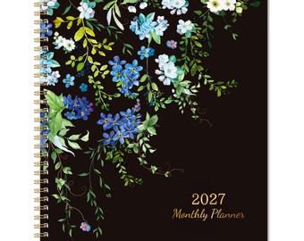 May include: A spiral-bound 2027 monthly planner featuring a black cover decorated with a watercolor-style illustration of blue and white flowers, green leaves, and thin vines cascading from the top left corner toward the center.
