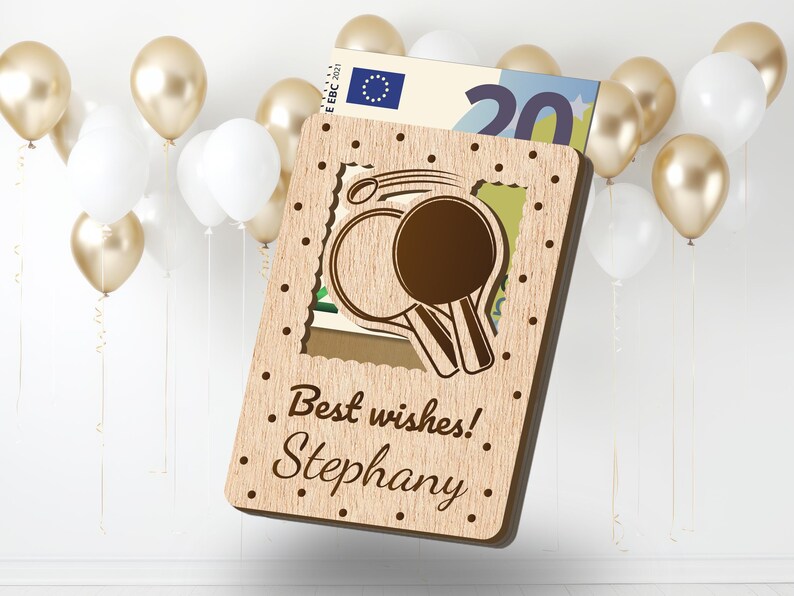 Pu&ograve; includere: Un biglietto di legno con un design ritagliato di due racchette da ping pong. Il biglietto ha il testo "I migliori auguri! Stephany." stampato su di esso.