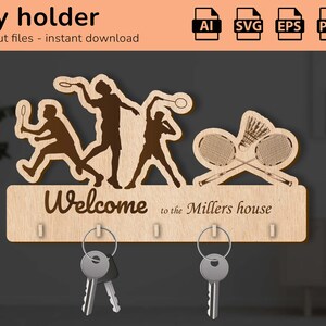 Pode incluir: Porta-chaves de madeira com silhuetas de jogadores de badminton e raquetes. Inclui o texto "Welcome to the Millers house" e ganchos para chaves. O porta-chaves é feito de madeira clara.