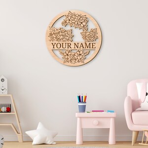 May include: A wooden round sign with a floral design and the text "YOUR NAME" in the center. The sign is light brown and has a natural wood finish.
