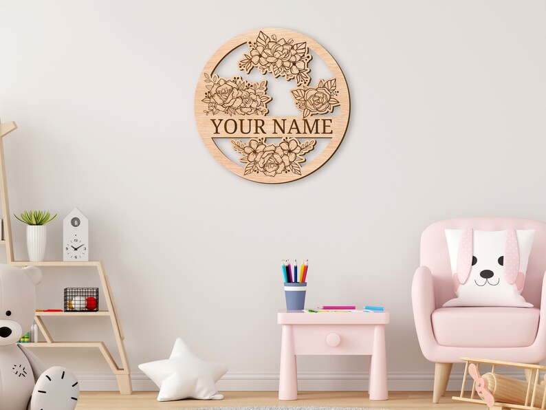 May include: A wooden round sign with a floral design and the text "YOUR NAME" in the center. The sign is light brown and has a natural wood finish.