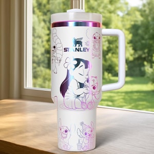 May include: White Stanley tumbler featuring a handle and a screw-on lid. The tumbler is decorated with illustrations of Lilo and Stitch in a colorful, iridescent design. The Stanley logo is also visible.