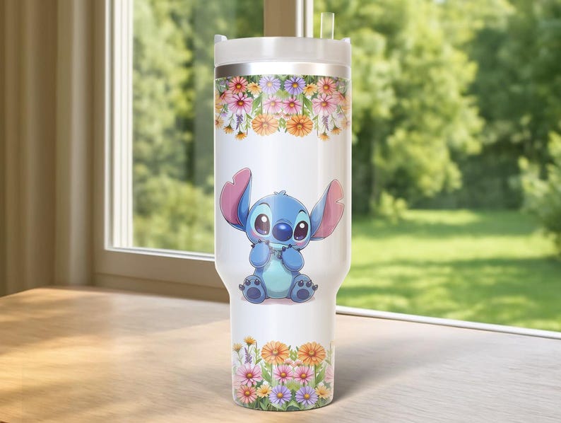 Pu&ograve; includere: Un bicchiere bianco con un'immagine a cartoni animati di Stitch, decorato con motivi floreali. Il bicchiere ha un coperchio bianco e una cannuccia trasparente. Il design floreale comprende fiori rosa, arancioni e gialli. Lo sfondo &egrave; una scena esterna verde sfocata.