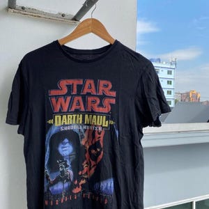 May include: Black Star Wars t-shirt featuring Darth Maul. The shirt has a graphic of Darth Maul with the Star Wars logo in red and white. The text "SHADDI J. HUNTER" and "MICHAEL REEVES" are also visible.