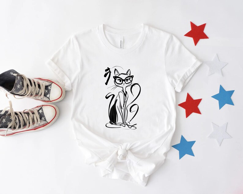 May include: White t-shirt featuring a black and white illustration of a cat wearing glasses. The cat design is accompanied by Japanese characters. The shirt is paired with high-top sneakers and star-shaped decorations in red, white, and blue.