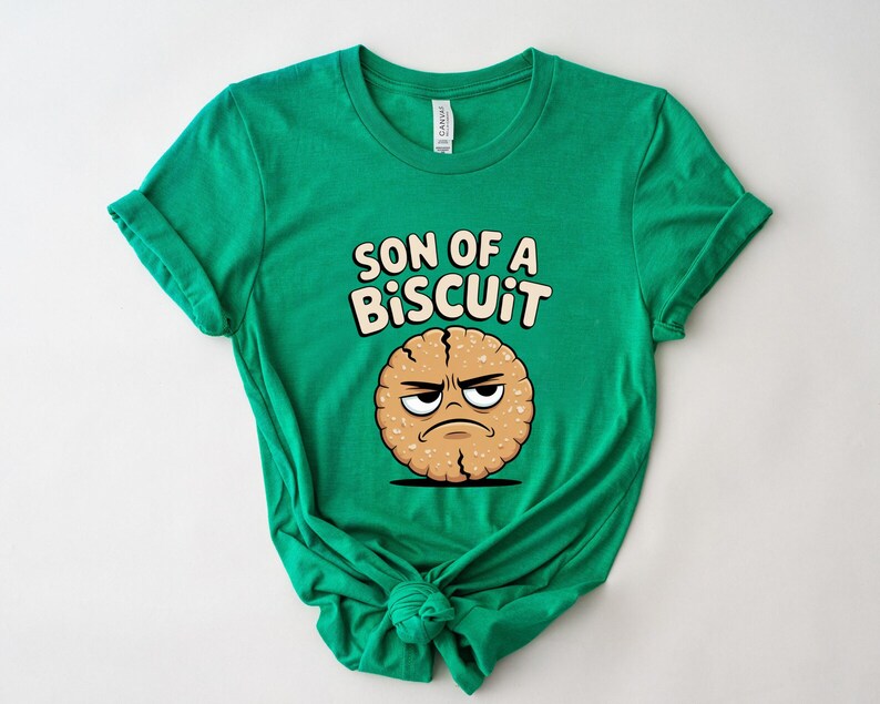 May include: A bright green t-shirt featuring the phrase "SON OF A BISCUIT" above a cartoon biscuit with an angry expression. The biscuit is light brown with a cracked texture and a black outline.