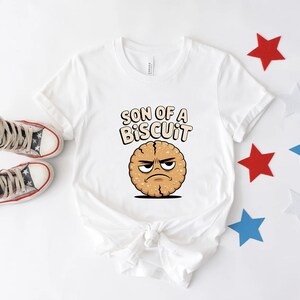 May include: White t-shirt with the phrase "SON OF A BISCUIT" and a cartoon biscuit with an angry face. The shirt is paired with high-top sneakers and star-shaped decorations in red, white, and blue.