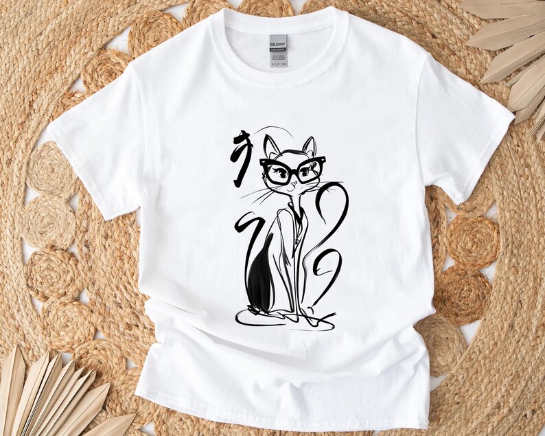 May include: White t-shirt featuring a black and white illustration of a cat wearing glasses. The cat is drawn in a minimalist style with long, flowing lines. The shirt also has Japanese characters above the cat.