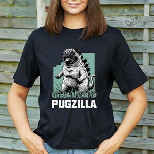 May include: Black t-shirt with a graphic of a pugzilla, a pug with a Godzilla-like pose, on a green background. The text "PUGZILLA" is printed below the graphic.