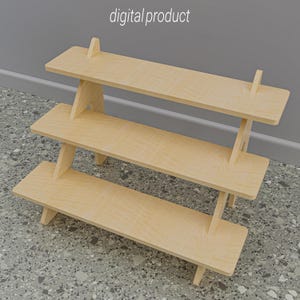 Puede incluir: Estantería de madera de tres niveles con acabado de madera clara. Los estantes están soportados por patas anguladas y soportes verticales en la parte trasera. El texto "digital product" está en la parte superior. Diseñado para exhibir artículos.