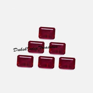 Puede incluir: Seis gemas rectangulares de color rojo intenso dispuestas sobre un fondo blanco. Las gemas tienen una superficie pulida y reflectante. El texto "Daksh India Treasures" está en la esquina inferior izquierda. Estas gemas podrían usarse para hacer joyas.