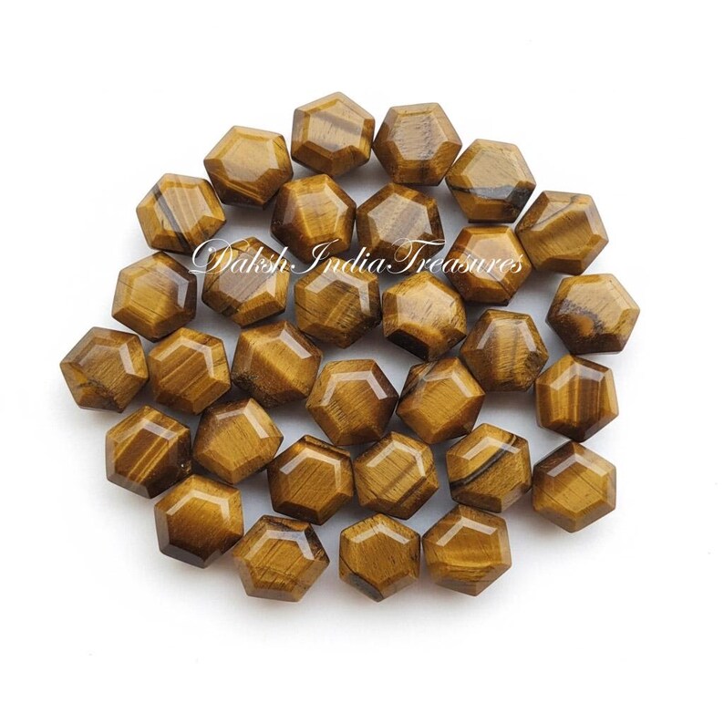 May include: A collection of faceted, hexagonal tiger's eye gemstones. The stones are a warm brown color with darker brown stripes and patterns. The text "Daksh India Treasures" is visible on the image.