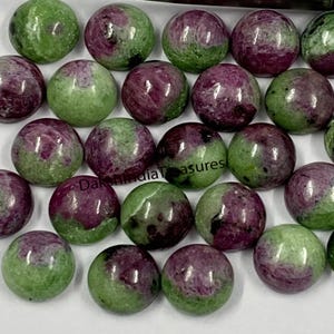 May include: A collection of 20 round, cabochon cut gemstones. The stones are a mix of green and pink, with some having a more pronounced pink hue. The stones are all approximately the same size and shape.