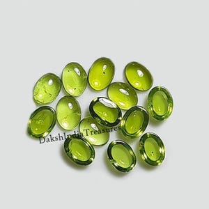 May include: A collection of 12 oval-shaped green gemstones. The gemstones are smooth and polished, with a translucent appearance.