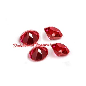 K&ouml;nnte beinhalten: Vier facettierte, ovale und runde, tiefrote Edelsteine. Die Edelsteine sind auf wei&szlig;em Hintergrund angeordnet. Der Text "Daksh India Treasures" ist in Kursivschrift in der linken unteren Ecke geschrieben.