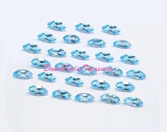 May include: A collection of oval-cut, light blue gemstones arranged on a white surface. The gemstones are faceted, reflecting light, and appear to be of uniform size and shape. The image is well-lit, highlighting the clarity and color of the stones.