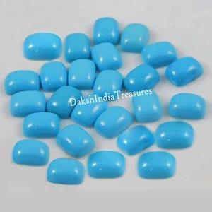 May include: A collection of 25 turquoise cabochons, each with a smooth, polished surface. The stones are a vibrant blue colour and are all approximately the same size and shape.