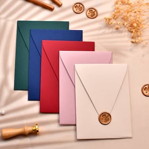 May include: Five envelopes in different colors, including green, blue, red, pink, and beige, are arranged in a stack. Each envelope has a decorative wax seal with a floral design.
