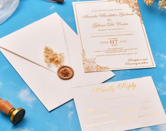 May include: Wedding invitation suite with a cream-colored envelope, invitation, and reply card. The invitation features gold floral accents and text. A wax seal and dried flowers adorn the envelope. The invitation includes the names Imashi Panditha Gedara and Gihan De Costa.
