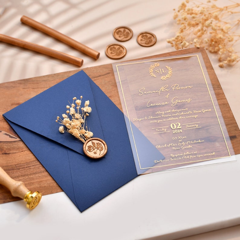May include: A clear acrylic wedding invitation with gold lettering. The invitation features the names Samantha Pereira and Lorenzo Gamis, the date Tuesday, January 02, 2024, and the time 03:30 pm. The invitation also includes the location, Church of Our Lady of the Assumption, and the reception location, Dorchester Country Club, open bar.