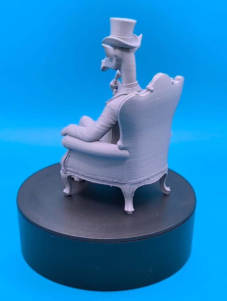 May include: A light gray 3D printed figurine of an anthropomorphic giraffe wearing a top hat and a suit, sitting in a detailed armchair. The figure is depicted in profile, holding a small pipe near its mouth, showcasing a smooth, matte finish.