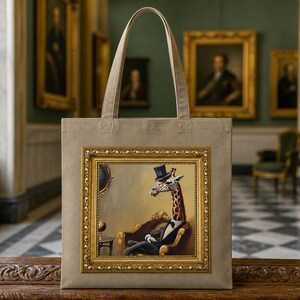 May include: A beige canvas tote bag featuring a rectangular print of a giraffe wearing a black top hat, a white shirt, and a black tuxedo jacket, seated in a chair. The print is enclosed within a decorative gold-colored ornate frame.