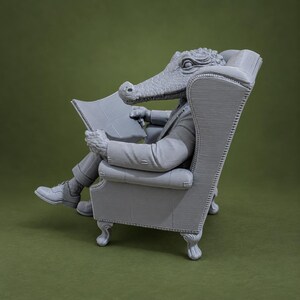 May include: A gray 3D printed figurine of an anthropomorphic crocodile wearing a suit and sitting in a high-backed wingback chair while holding an open newspaper. The figure features textured skin, formal attire, and detailed furniture upholstery.