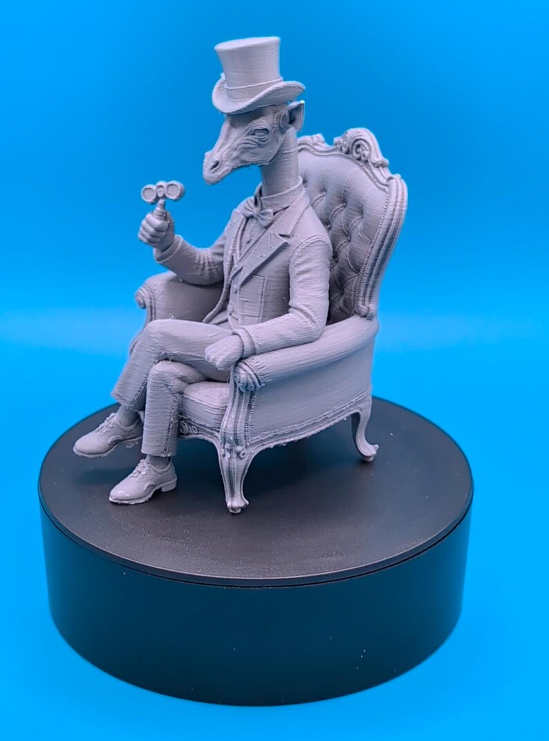 May include: A light gray 3D printed figurine of a giraffe with a human-like body wearing a formal suit, a bow tie, and a top hat. The giraffe is seated in a tufted armchair, holding a small mechanical device in one hand, with its legs crossed.