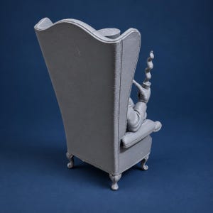 Puede incluir: Una figura gris monocrom&aacute;tica impresa en 3D de un personaje sentado en un sill&oacute;n de respaldo alto. El personaje sostiene una pipa con una columna de humo visible que se eleva. El sill&oacute;n presenta reposabrazos curvos y patas cabriol&eacute; ornamentadas.