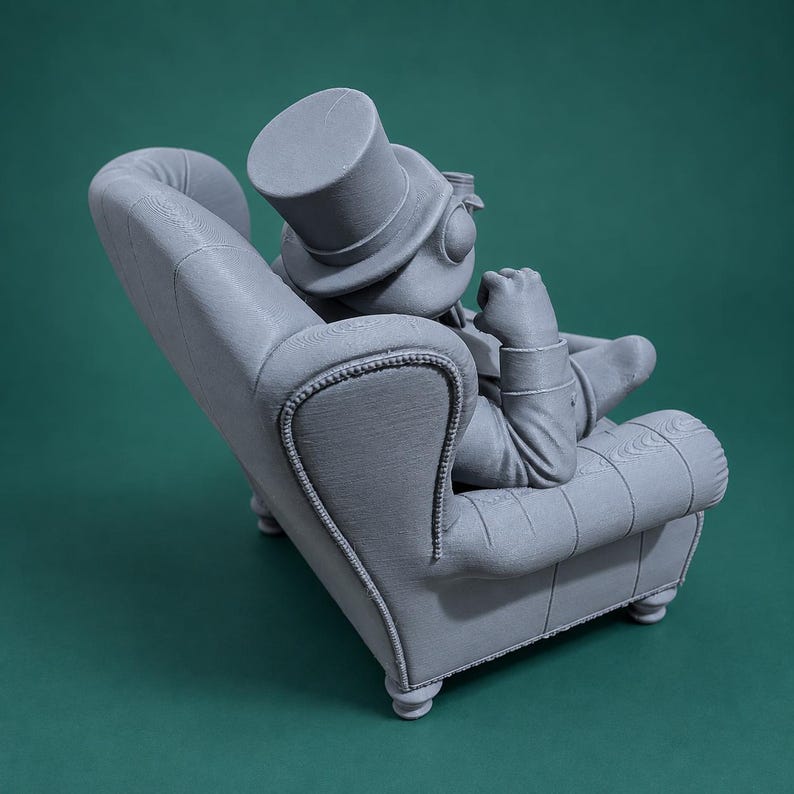 May include: A monochromatic gray 3D printed figurine of a frog wearing a top hat and formal attire, seated in a detailed armchair. The frog is positioned with one hand resting near its chin, showcasing textured surfaces and visible layer lines.