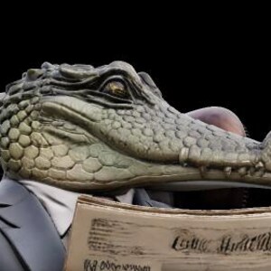 May include: A sculpture of an alligator head wearing a suit and reading a newspaper. The alligator is seated in a brown leather chair against a black background. The newspaper reads "The Watchful Herald".