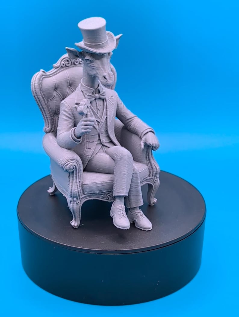 May include: A monochromatic gray 3D printed figurine of an anthropomorphic giraffe wearing a top hat, a formal suit with a vest, and a bow tie. The giraffe is seated in an ornate, tufted high-back armchair, holding a small hammer in one hand.