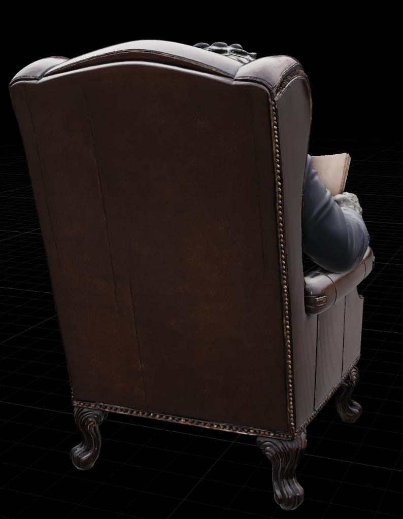May include: A dark brown leather armchair with a high back and scrolled legs. The chair has a classic design with a tufted back and armrests. The back of the chair is visible, with a person in a blue jacket and white cuffs reading a book.