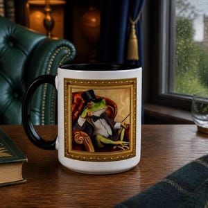 May include: A white ceramic mug with a black handle and interior, featuring a rectangular gold-framed illustration of a green frog wearing a black top hat, a white shirt, a black bowtie, and a black jacket while sitting in a red armchair.