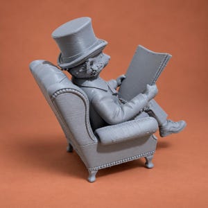 May include: A gray 3D printed figurine of an anthropomorphic bear wearing a top hat and formal attire, seated in a tufted armchair while holding an open newspaper. The bear is depicted in profile, showing detailed textures on the chair and clothing.