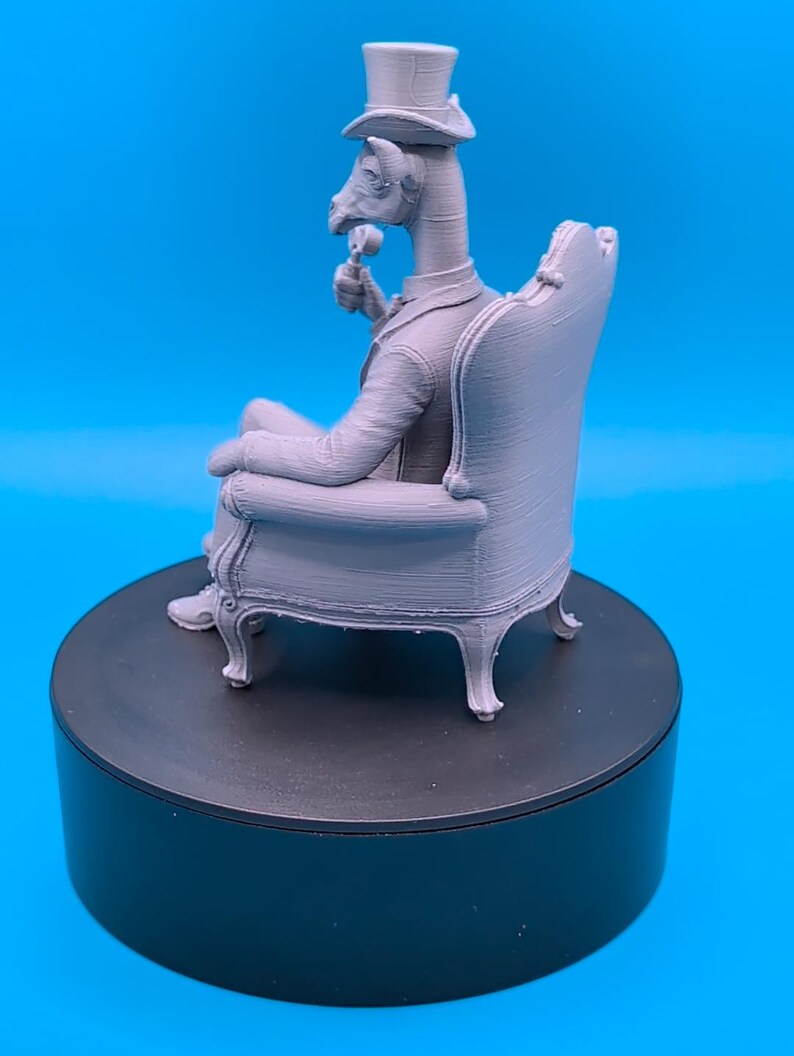 May include: A light gray 3D printed figurine of an anthropomorphic goat wearing a formal suit and a top hat, sitting in an ornate armchair while holding a small circular object. The figure is rendered in a monochromatic matte finish.