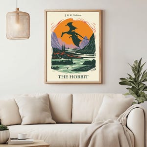May include: A vintage-style poster for "The Hobbit" by J.R.R. Tolkien. The poster features a black silhouette of a dragon flying over a landscape with a river and mountains. The background is a sunset with orange, yellow, and purple hues.