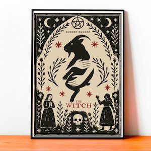Puede incluir: Póster enmarcado en negro con una ilustración estilizada de la película "The Witch". La obra de arte incluye una cabra negra abrazada por manos, estrellas rojas, medias lunas y el texto "THE WITCH" y "ROBERT EGGERS".