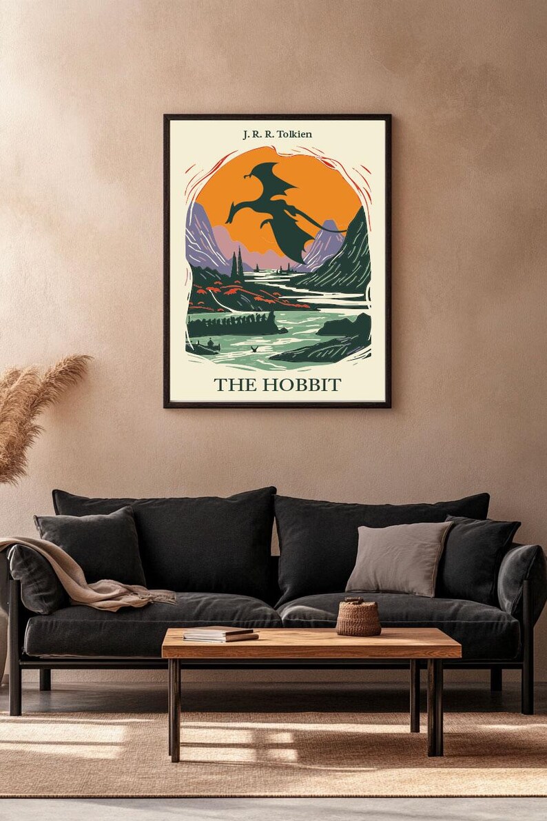 May include: A vintage-style poster for "The Hobbit" by J.R.R. Tolkien. The poster features a silhouette of a dragon flying over a landscape with mountains, a river, and trees. The poster has a cream background with black text and a black frame.