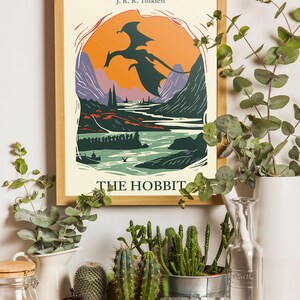 May include: A framed poster with a vintage illustration of a dragon flying over a landscape. The poster is titled "The Hobbit" and features the author's name, J.R.R. Tolkien.