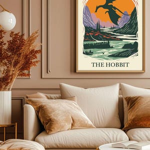 May include: A vintage-style poster for the book "The Hobbit" by J.R.R. Tolkien. The poster features a green, orange, and purple landscape with a black dragon flying over a river. The text "THE HOBBIT" is printed in black at the bottom of the poster.