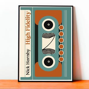 May include: A framed art print featuring a retro cassette tape design in teal, orange, and black. The text "Nick Hornby High Fidelity" is printed vertically on the left side of the print. The design has a mid-century modern aesthetic.