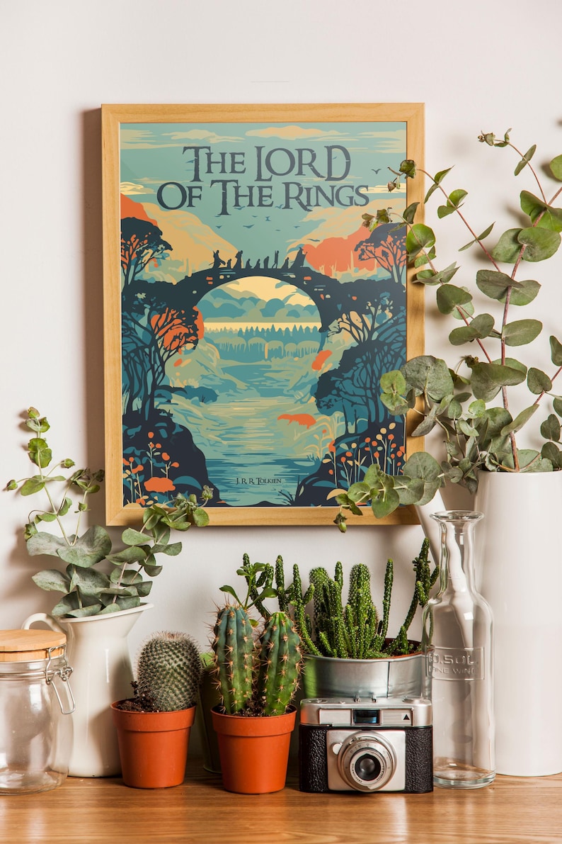 May include: A framed poster with a vintage illustration of a bridge and forest scene. The poster features the text "The Lord of the Rings" and "J.R.R. Tolkien". The poster is surrounded by plants and a camera.